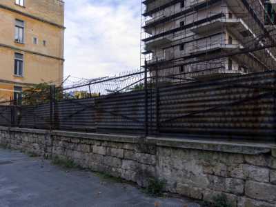 Ci avviciniamo al muro perimetrale, delimitato da blocchi di tufo e da una grata con filo spinato ormai totalmente arrugginita